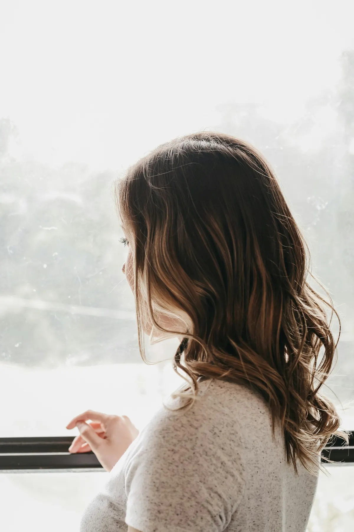 A woman looks out a misty window on a gray day.