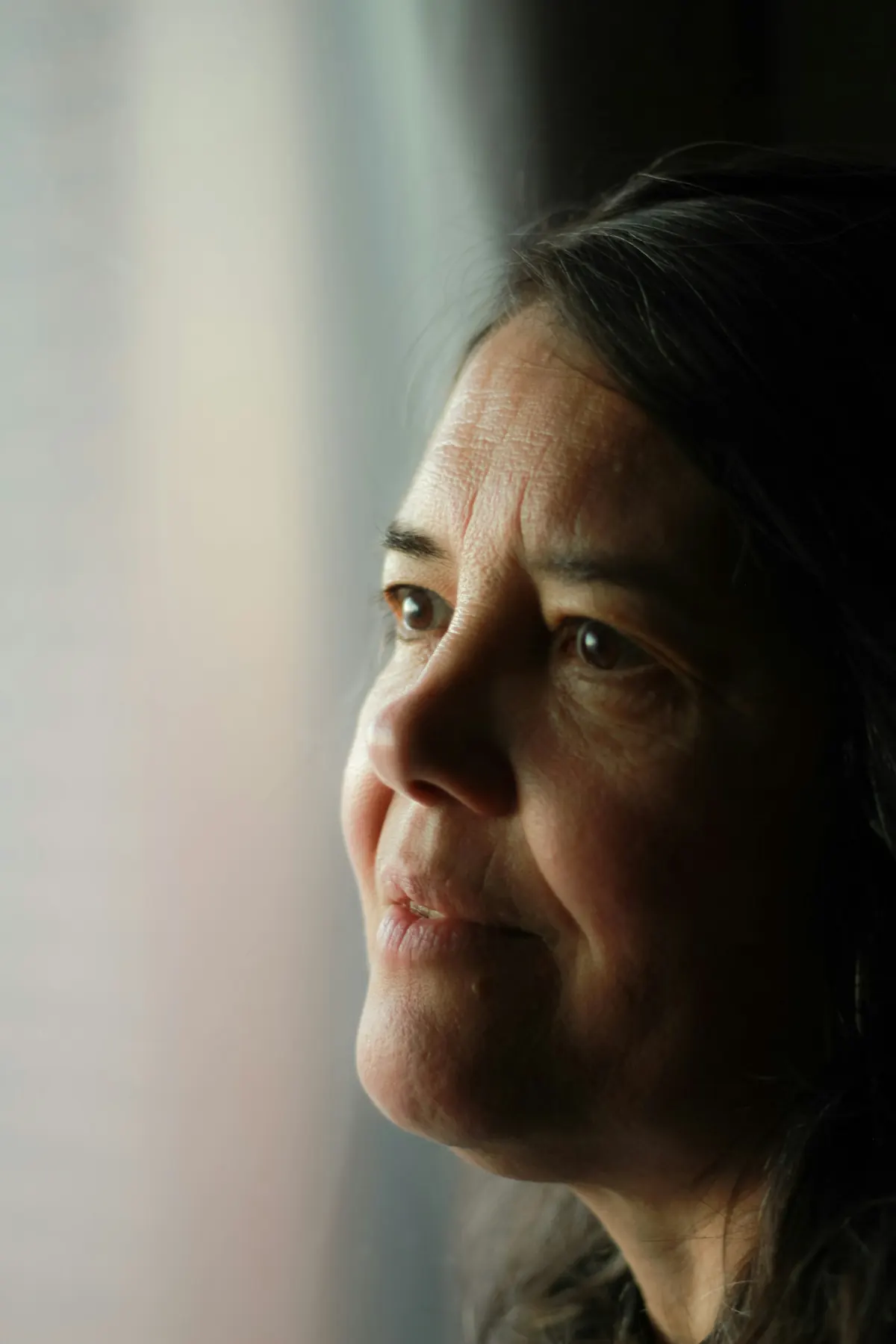 A woman in her forties looks out a window, calm and thoughtful.