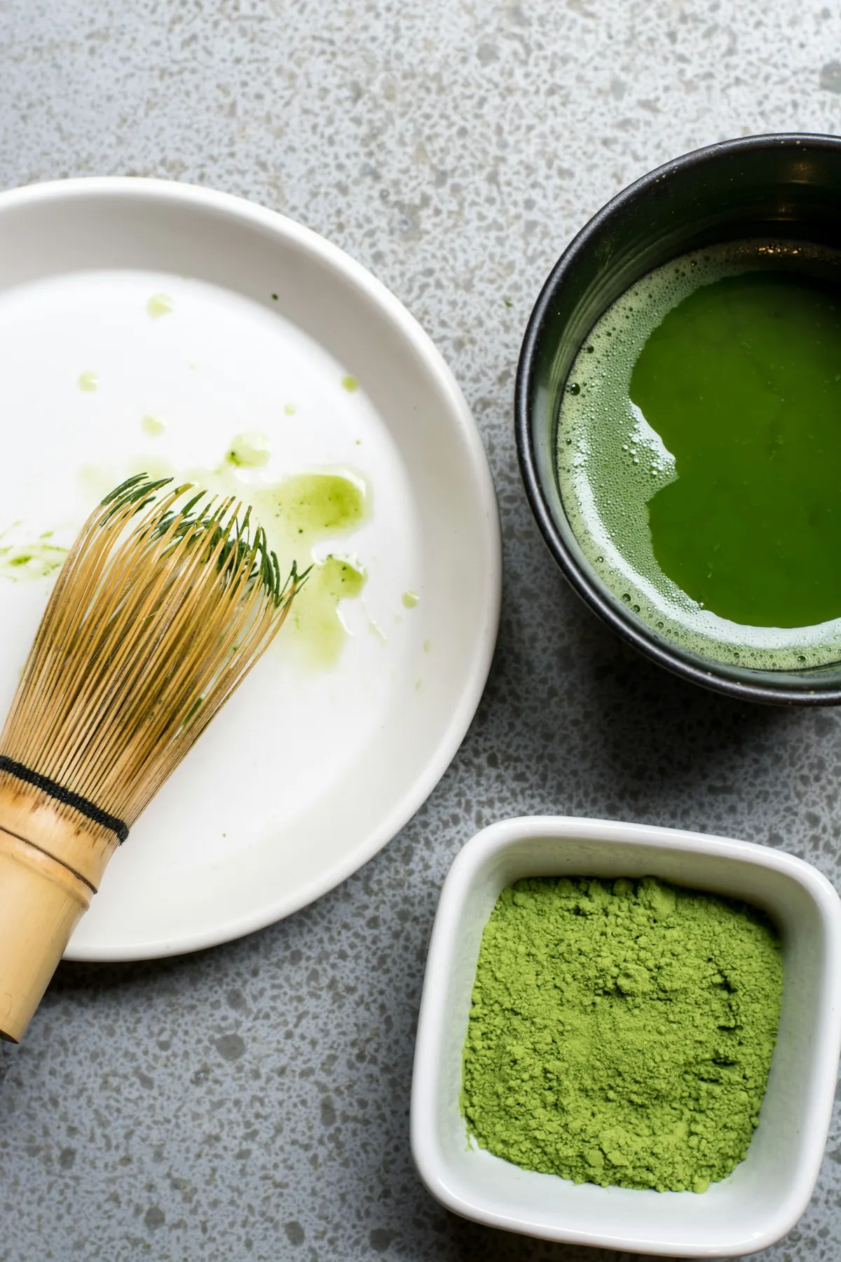 Matcha powder, a bamboo whisk and a bowl of green tea seen from above.